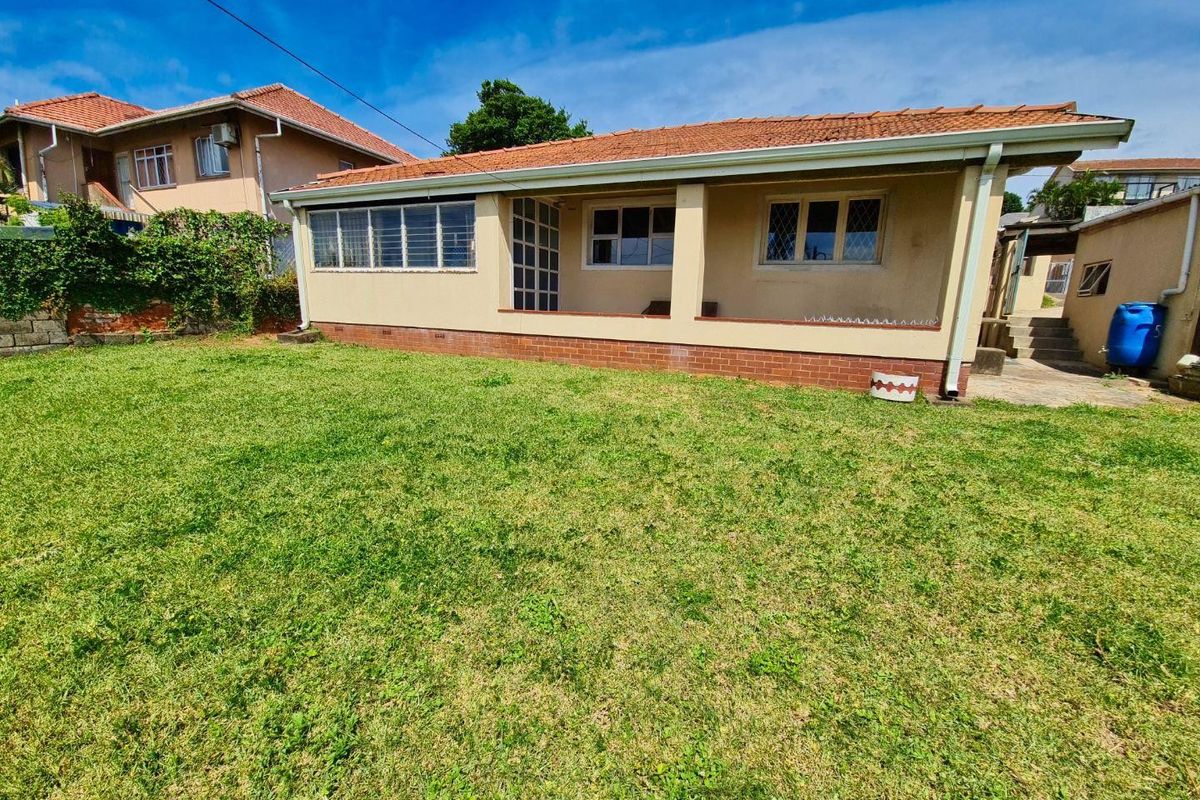 Rear view of the house featuring a covered patio area, terracotta roof tiles, and a spacious lawn.