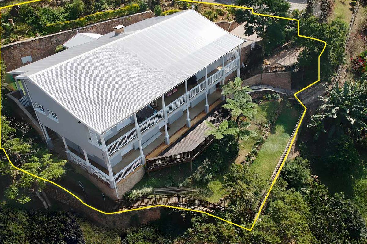 Aerial view of a multi-level townhouse featuring a metal roof, extensive timber decking, covered verandas, and landscaped garden areas with stone retaining walls.