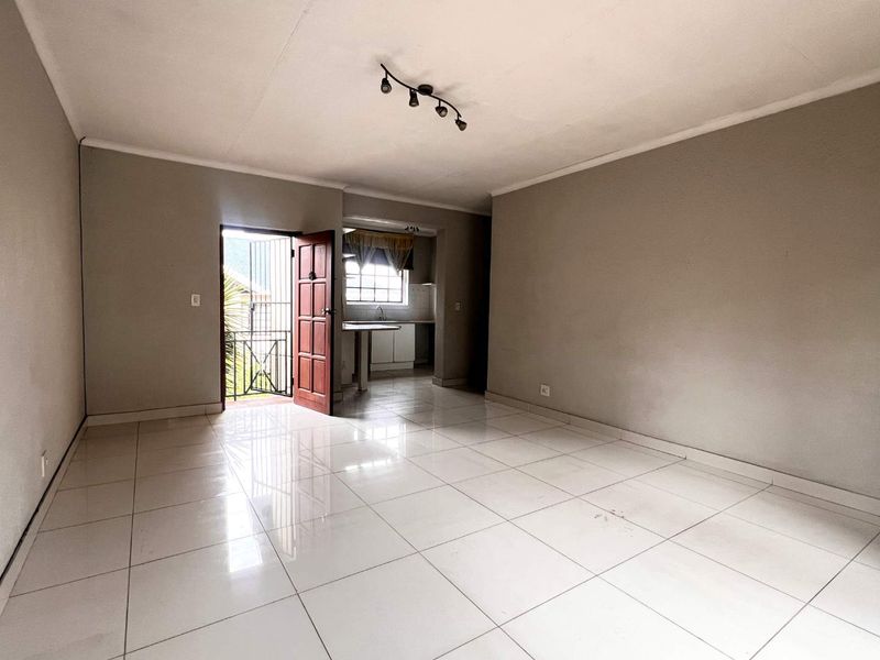 An open-plan living area featuring tiled flooring, track lighting, and an adjoining kitchen space with a breakfast counter and direct access to the exterior.