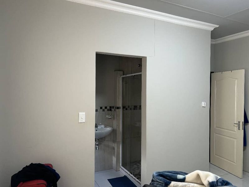 A bedroom featuring crown molding and a panel door, with an adjoining en-suite bathroom containing a shower enclosure and pedestal basin.