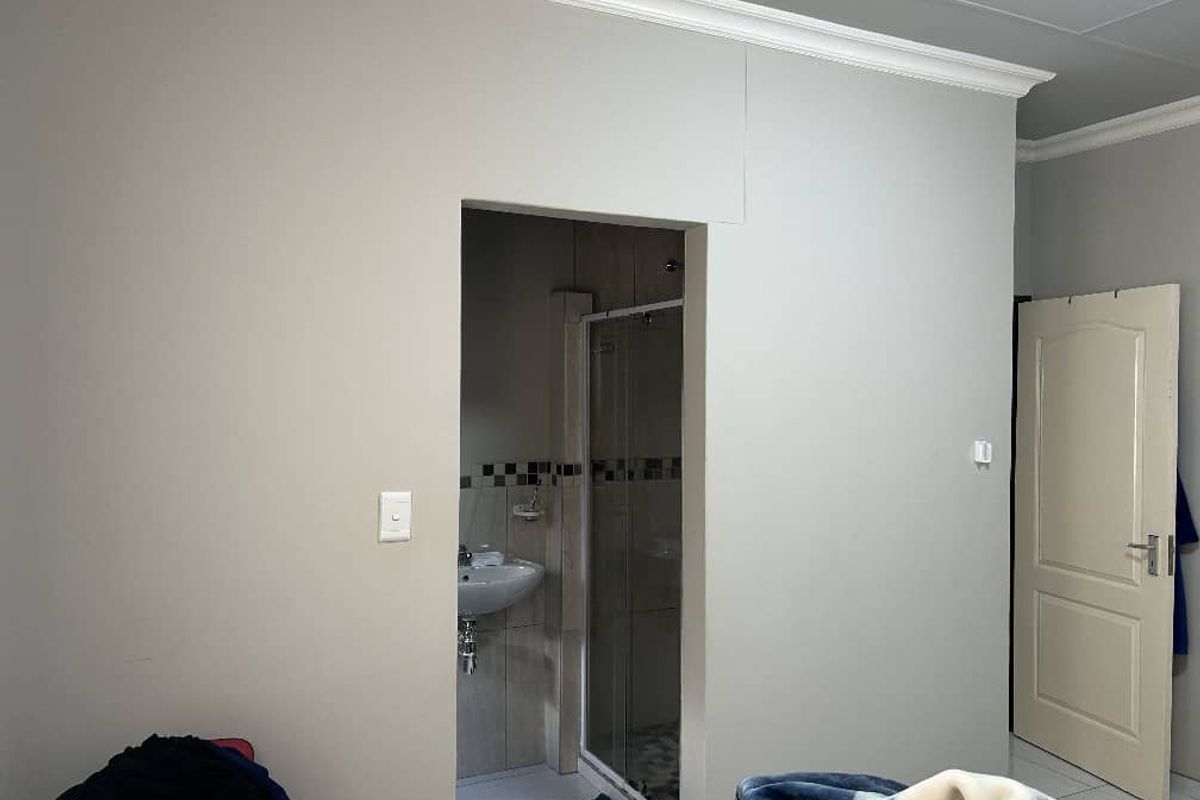 A bedroom featuring crown molding and a panel door, with an adjoining en-suite bathroom containing a shower enclosure and pedestal basin.