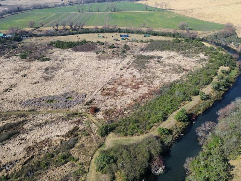 An aerial view of a large vacant residential plot featuring extensive open land, natural vegetation, and scenic river frontage.