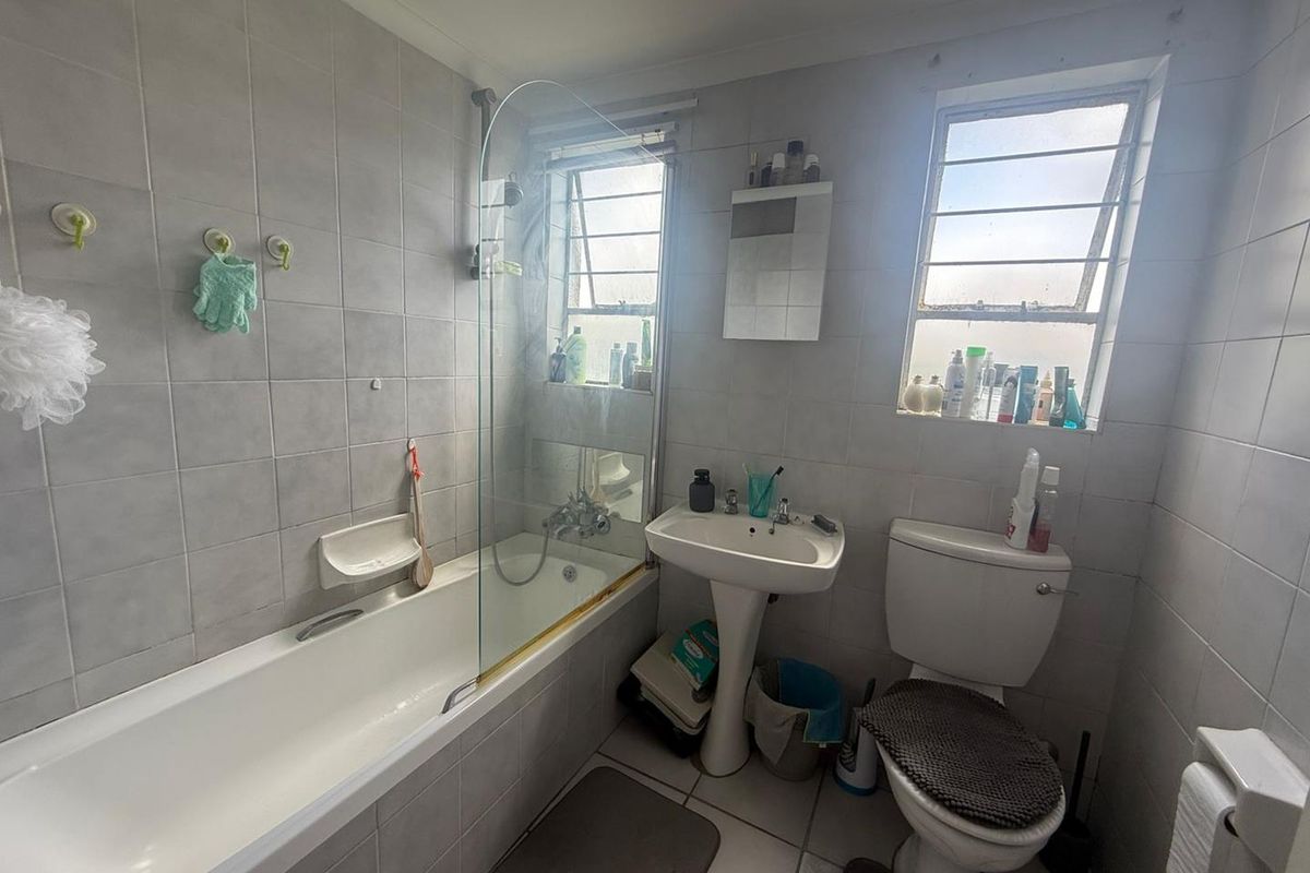 A functional bathroom featuring a bathtub with a glass screen, pedestal basin, and toilet, finished with neutral wall and floor tiling.