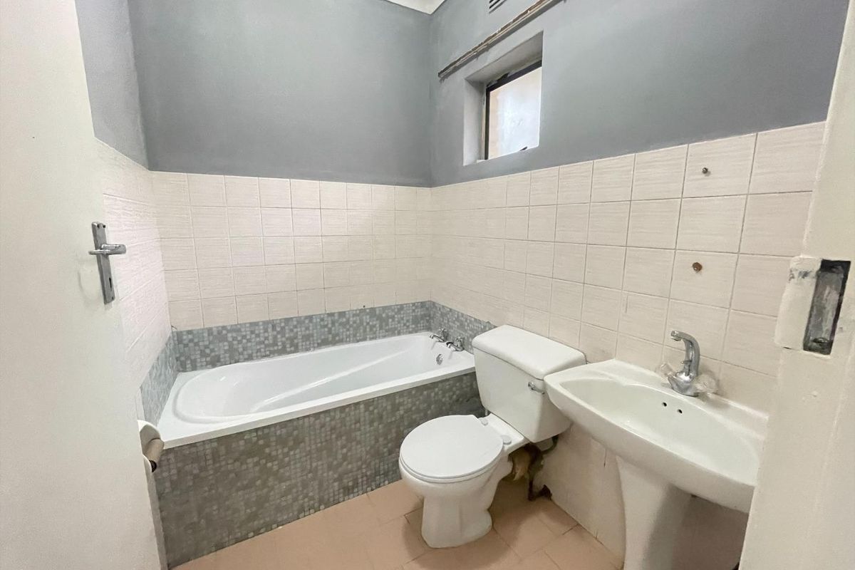 A functional bathroom featuring a bathtub, pedestal basin, and toilet, with tiled finishes and grey painted walls, requiring minor maintenance and cosmetic updates.