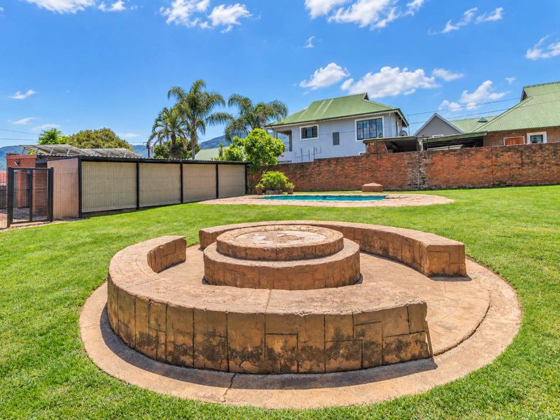 Spacious backyard featuring a well-maintained lawn, a swimming pool, and a large built-in circular brick fire pit area.