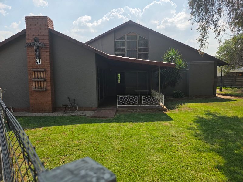 Rear view of the house featuring a brick chimney, a covered patio area, and a large feature window overlooking a well-maintained lawn.