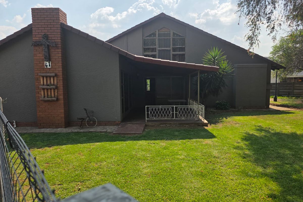 Rear view of the house featuring a brick chimney, a covered patio area, and a large feature window overlooking a well-maintained lawn.