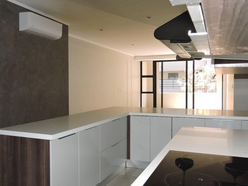 Modern kitchen featuring sleek cabinetry, stone countertops, integrated electric hob, extractor fan, and a split-system air conditioner, leading to an outdoor area.