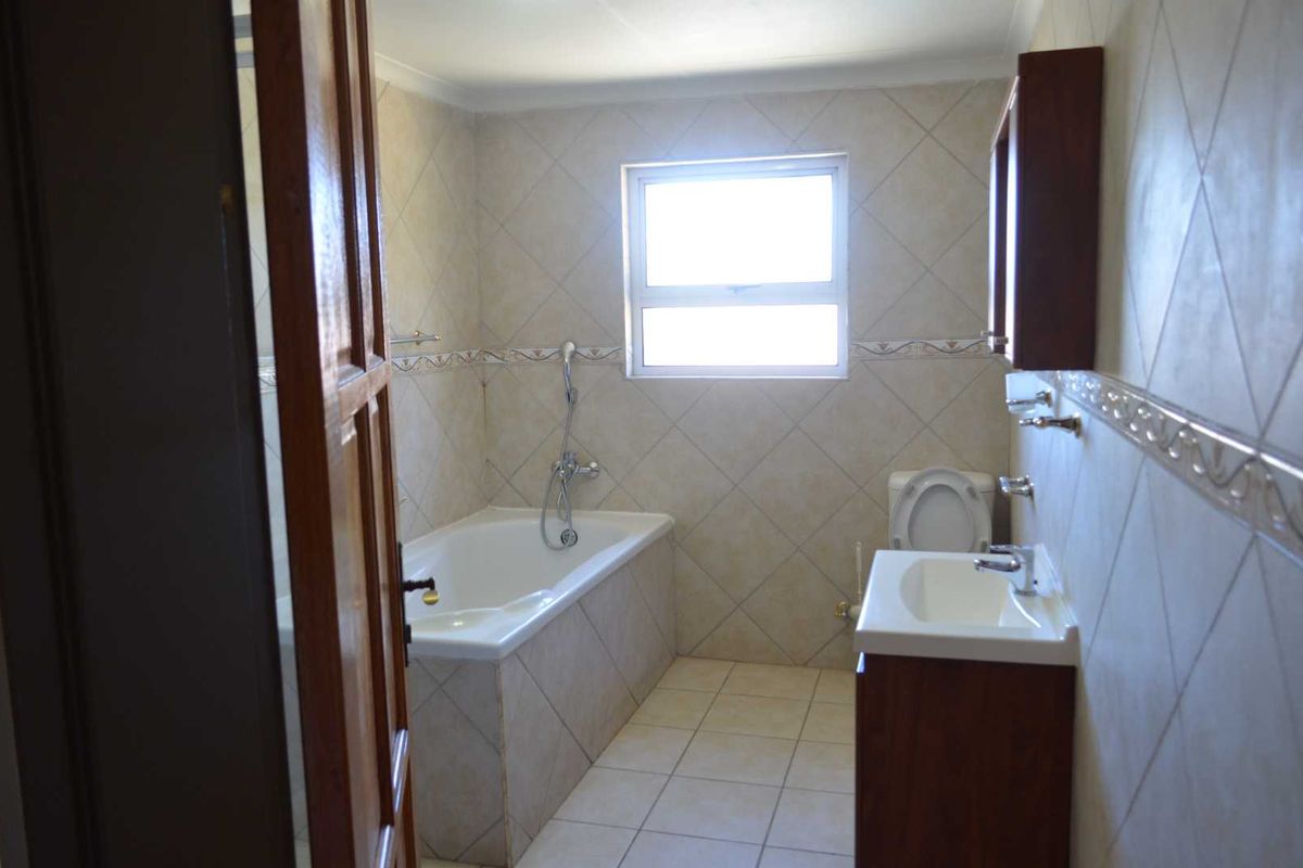 A functional bathroom featuring a built-in bathtub with shower mixer, a vanity basin, and a toilet, finished with neutral wall and floor tiling.