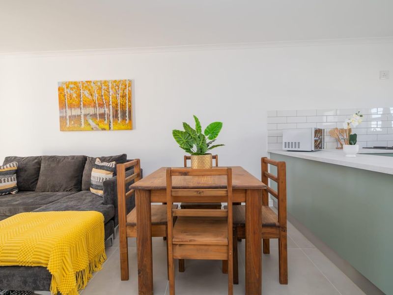A bright open-plan living and kitchen area featuring modern cabinetry, a subway tile backsplash, and neutral ceramic floor tiles.