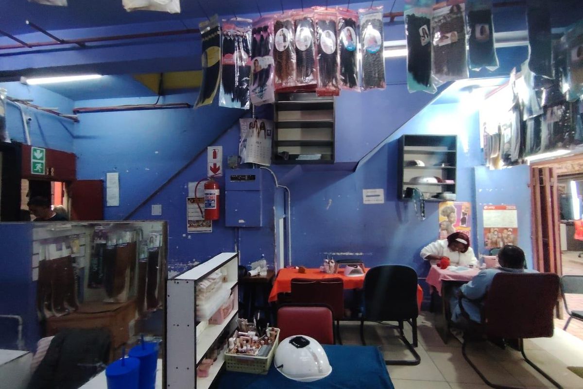 A retail space featuring blue painted walls, built-in shelving units, and exposed ceiling infrastructure, currently utilized as a salon or retail shop.