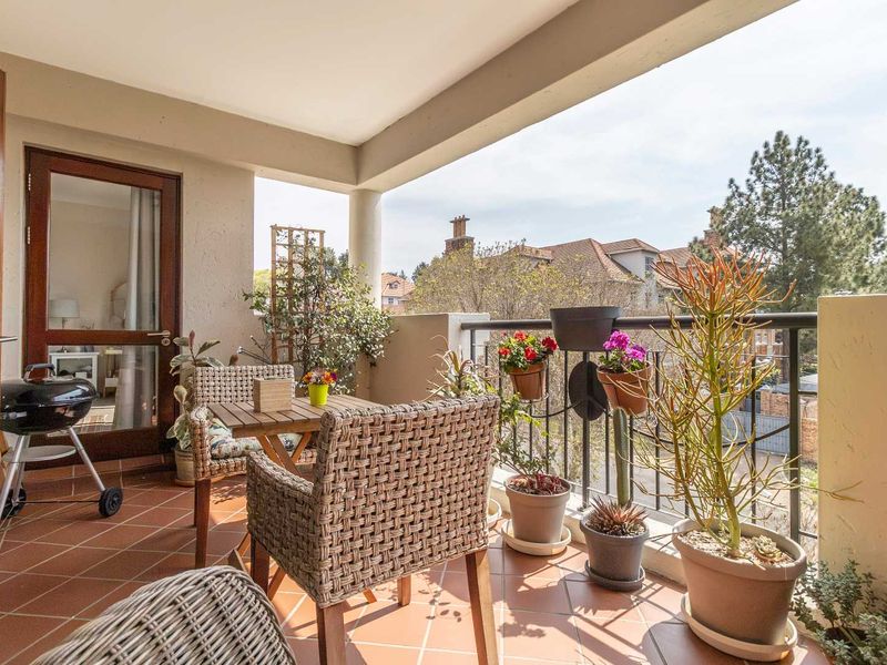 A covered balcony featuring terracotta tiled flooring and a metal balustrade, offering an outdoor space accessible through a glass door.