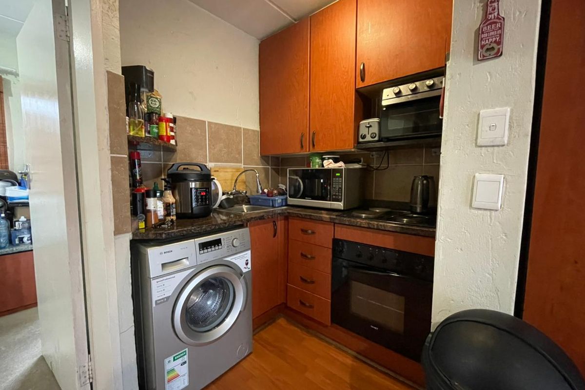 Compact kitchen featuring wood-finish cabinetry, built-in oven, hob, and integrated laundry appliance space with tiled backsplash.