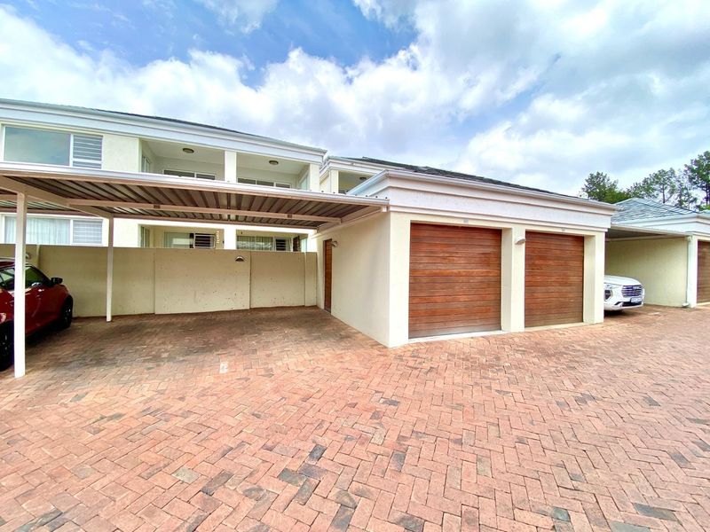 A well-maintained exterior view featuring a double garage with timber doors, a covered carport, and a paved driveway area.