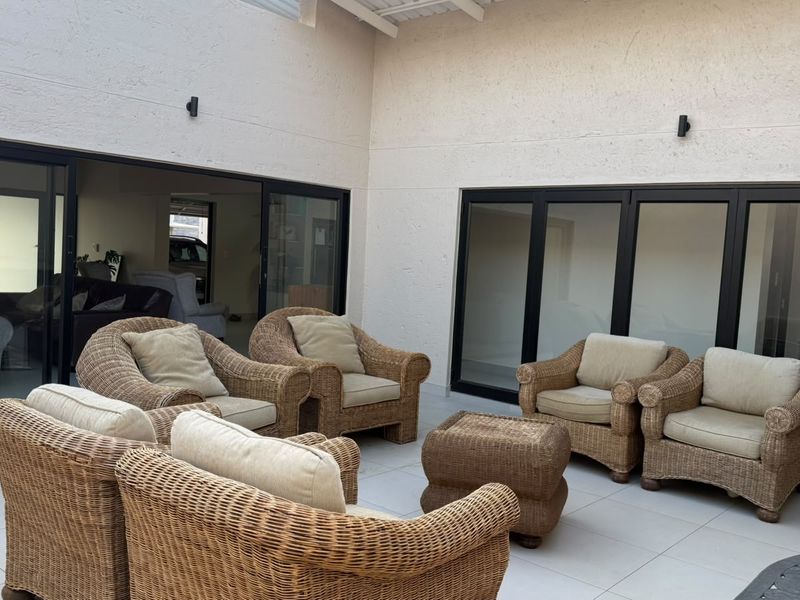 A spacious covered patio featuring large sliding glass doors, modern tiled flooring, and wall-mounted lighting, creating a seamless transition between indoor and outdoor living areas.