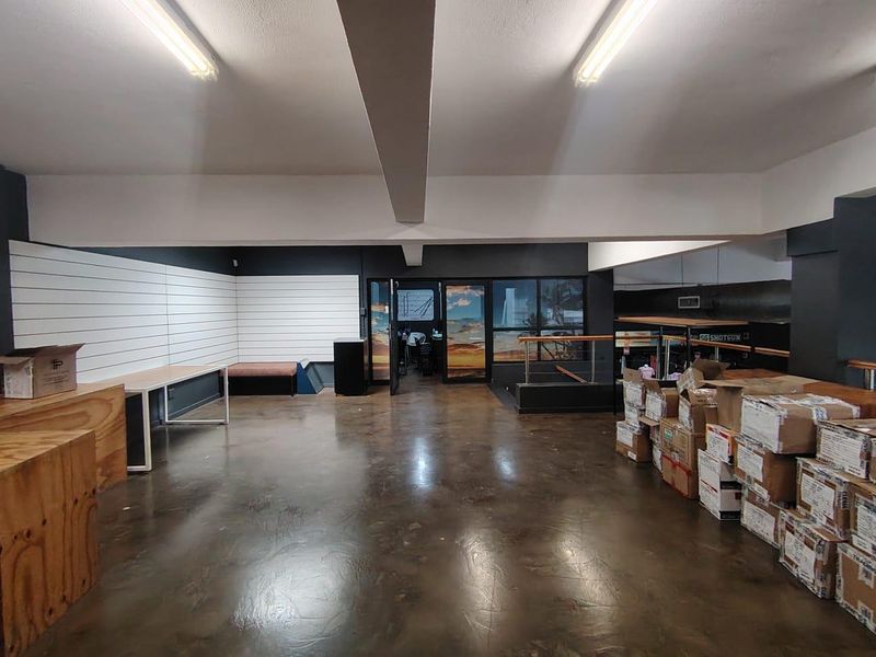 Spacious open-plan retail area featuring concrete flooring, slatwall display panels, and fluorescent lighting, suitable for various commercial business applications.