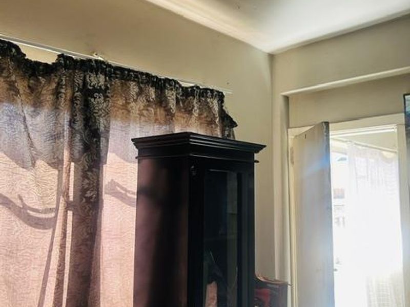 A bedroom interior featuring a window with a curtain rod and a doorway leading to an adjacent space.