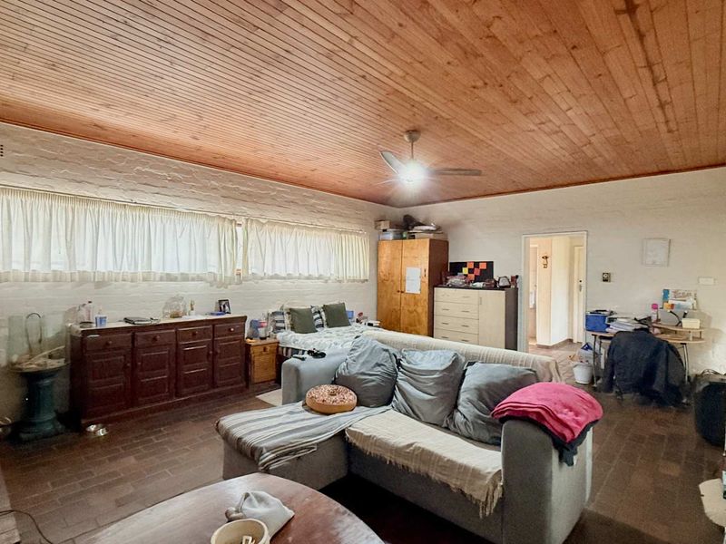Spacious living room featuring a warm timber-clad ceiling, textured brick walls, and durable tiled flooring, offering a comfortable and rustic living environment.
