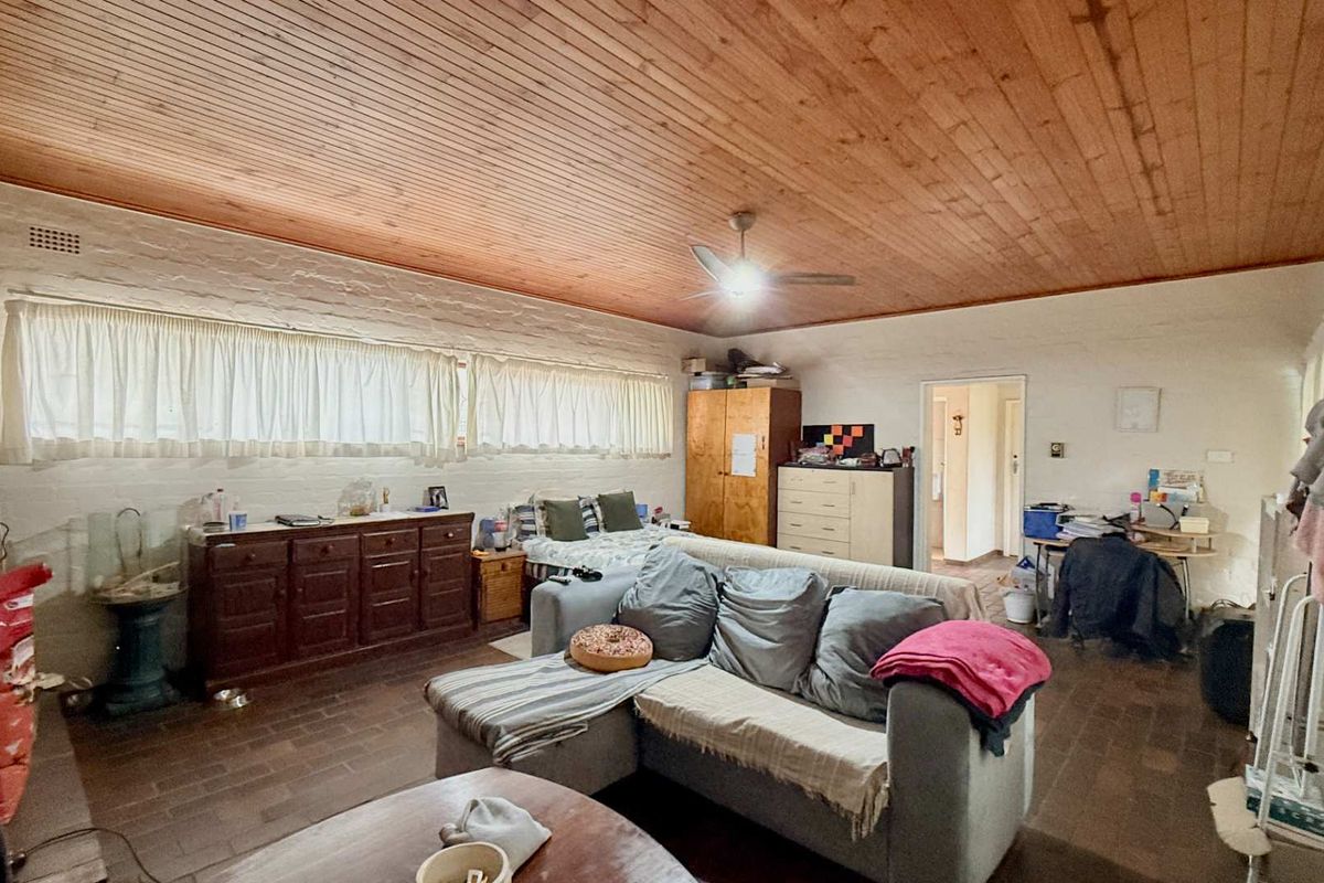 Spacious living room featuring a warm timber-clad ceiling, textured brick walls, and durable tiled flooring, offering a comfortable and rustic living environment.