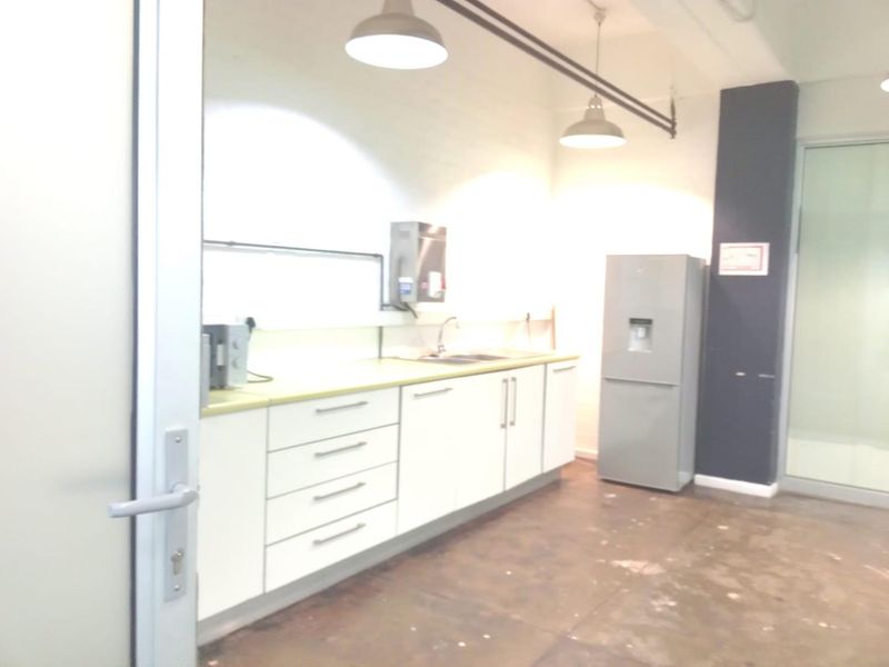 A functional office kitchenette featuring white cabinetry, a stainless steel sink, and industrial-style pendant lighting, set against a neutral backdrop.