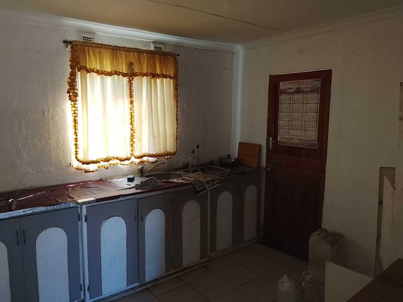 A dated kitchen featuring original built-in cabinetry, a stainless steel sink, and tiled flooring, requiring modernization to improve functionality and aesthetic appeal.