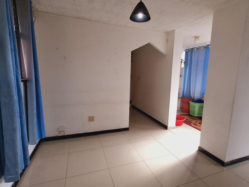 An empty living area featuring tiled flooring, a central pendant light, and an arched entryway leading to an adjacent space.