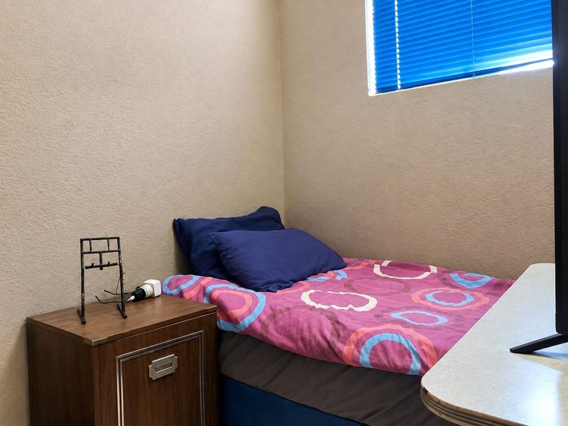 A compact bedroom featuring neutral wall finishes and a window fitted with blue venetian blinds.