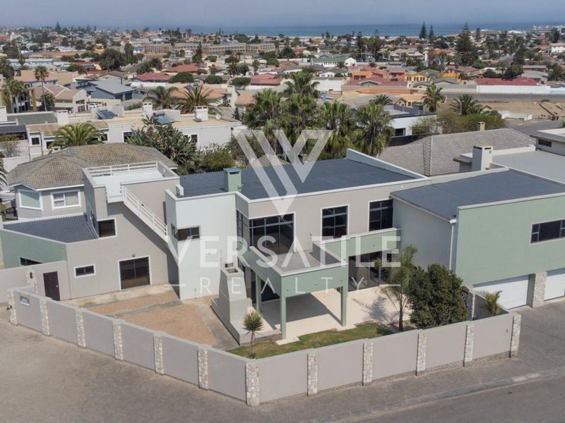 Aerial view of a modern multi-level residential property featuring a double garage, covered patio, and secure perimeter walling in a coastal neighborhood.