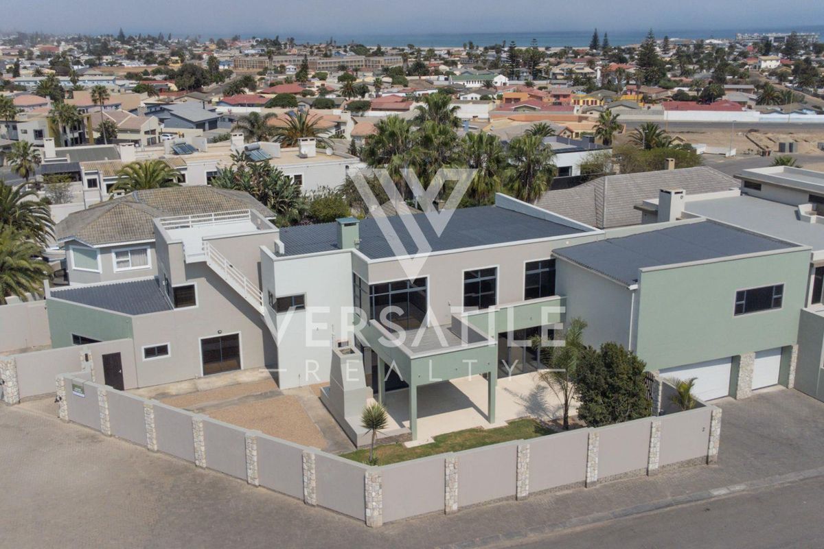 Aerial view of a modern multi-level residential property featuring a double garage, covered patio, and secure perimeter walling in a coastal neighborhood.