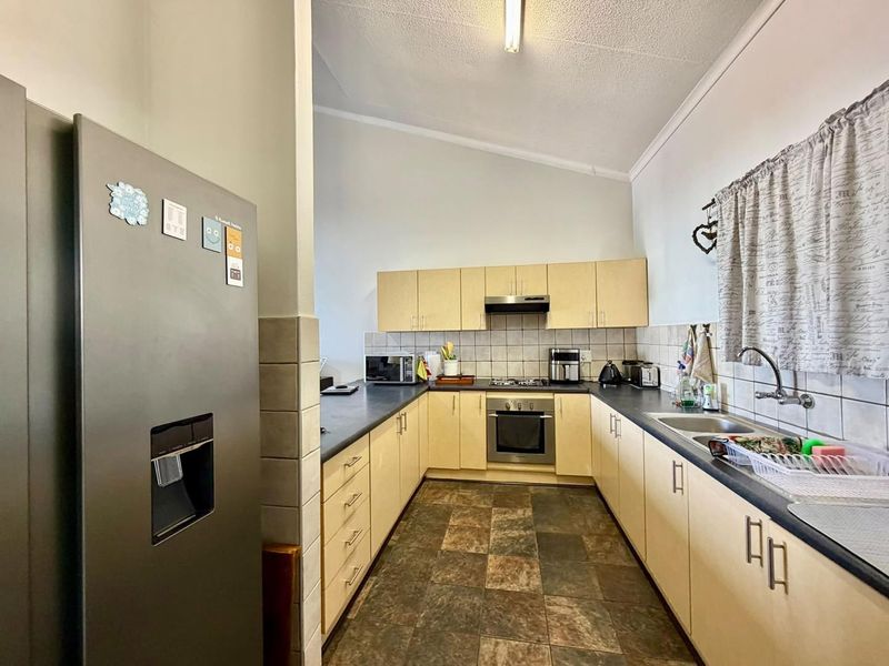 A functional U-shaped kitchen featuring light-toned cabinetry, dark laminate countertops, a built-in oven with gas hob, and tiled flooring.