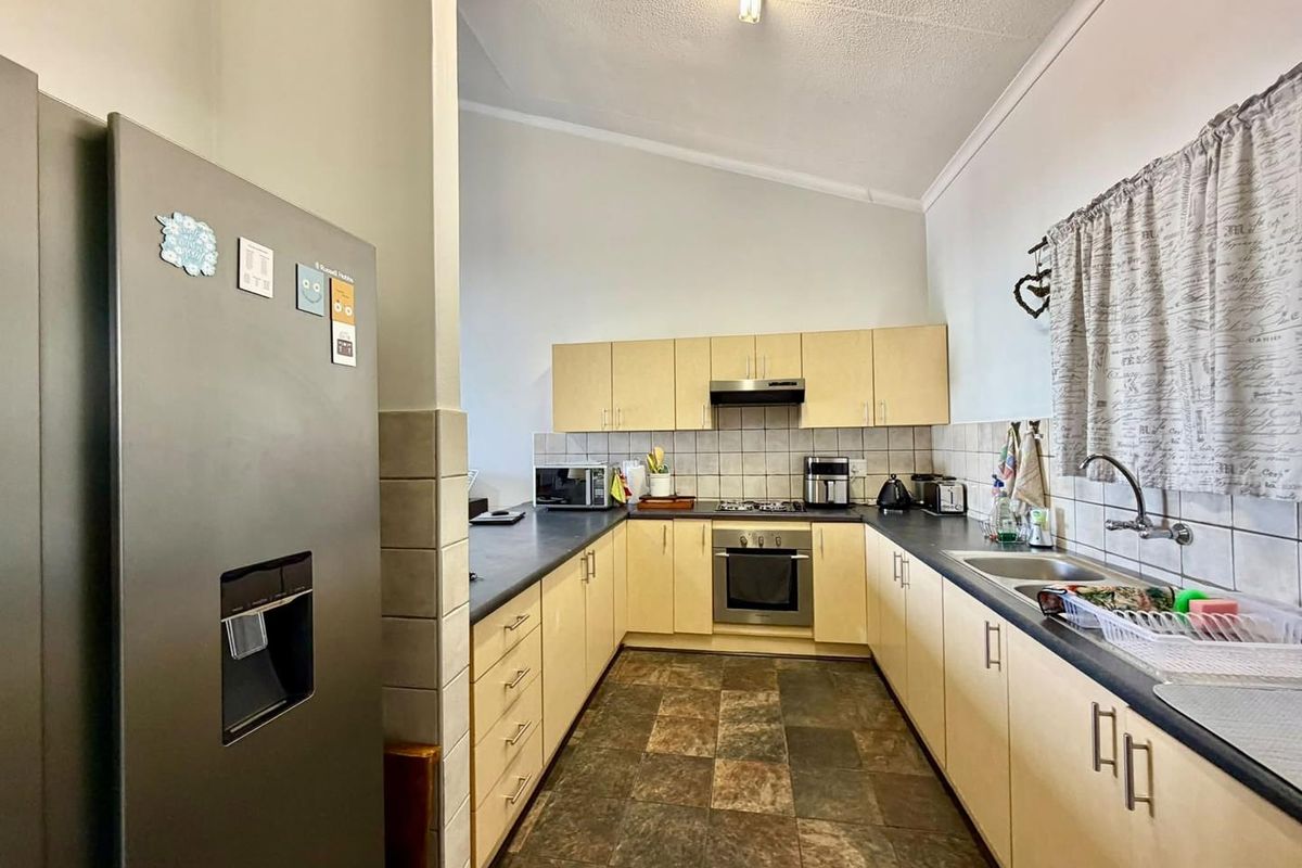 A functional U-shaped kitchen featuring light-toned cabinetry, dark laminate countertops, a built-in oven with gas hob, and tiled flooring.