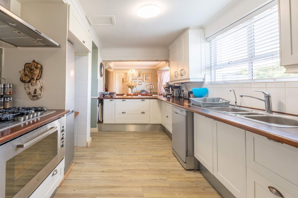 A well-maintained kitchen featuring white cabinetry, timber countertops, a built-in gas hob, oven, and stainless steel sink, flowing into an adjacent living area.