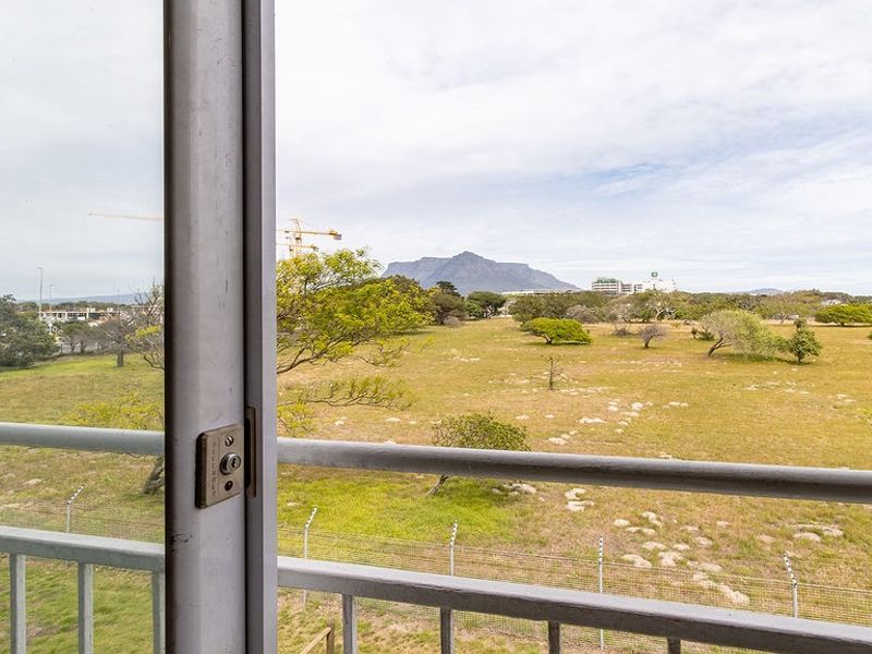 A scenic view of the surrounding landscape and mountain range, captured from a balcony with a metal railing and sliding door access.