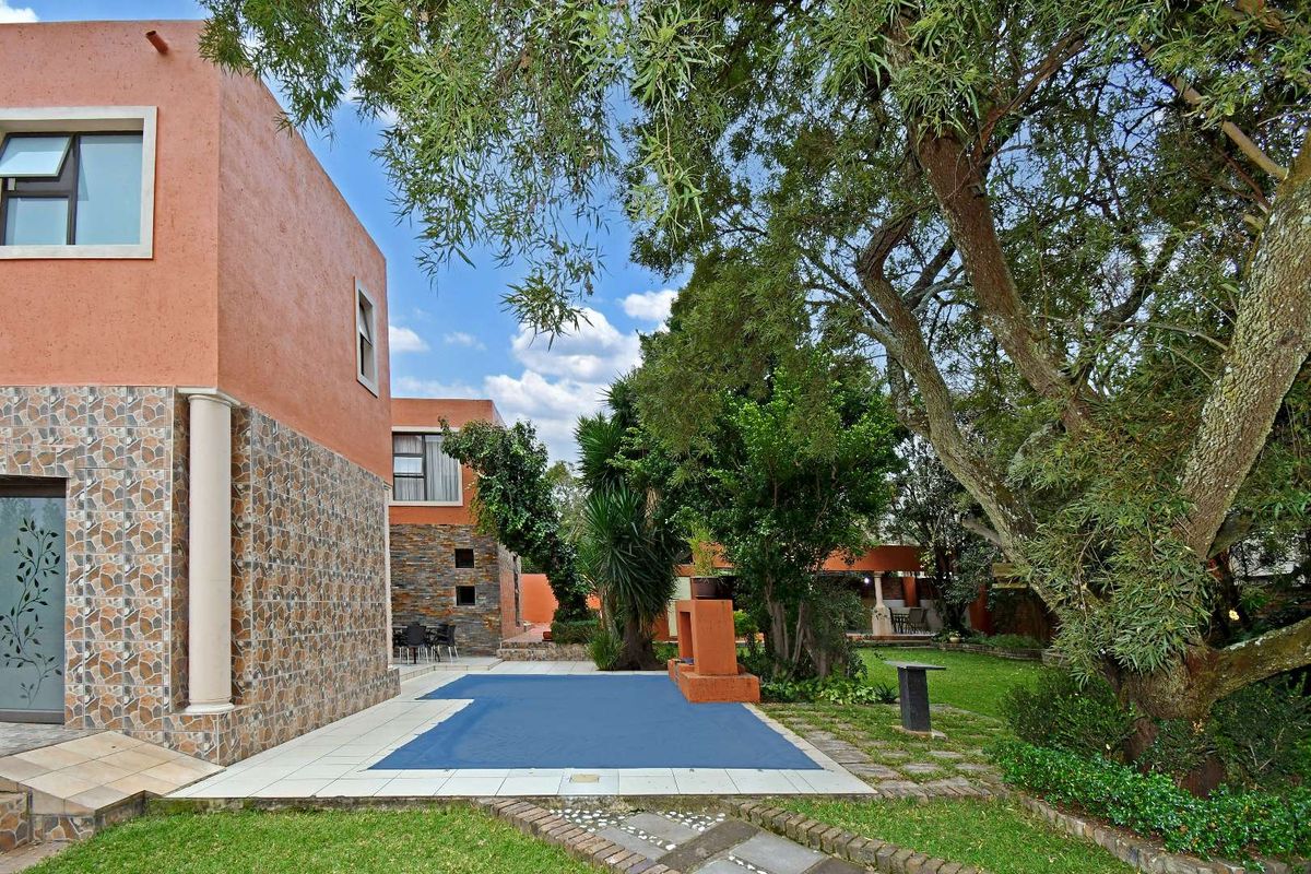 A rear garden area featuring a swimming pool with a cover, mature trees, and a paved patio area adjacent to the house structure.