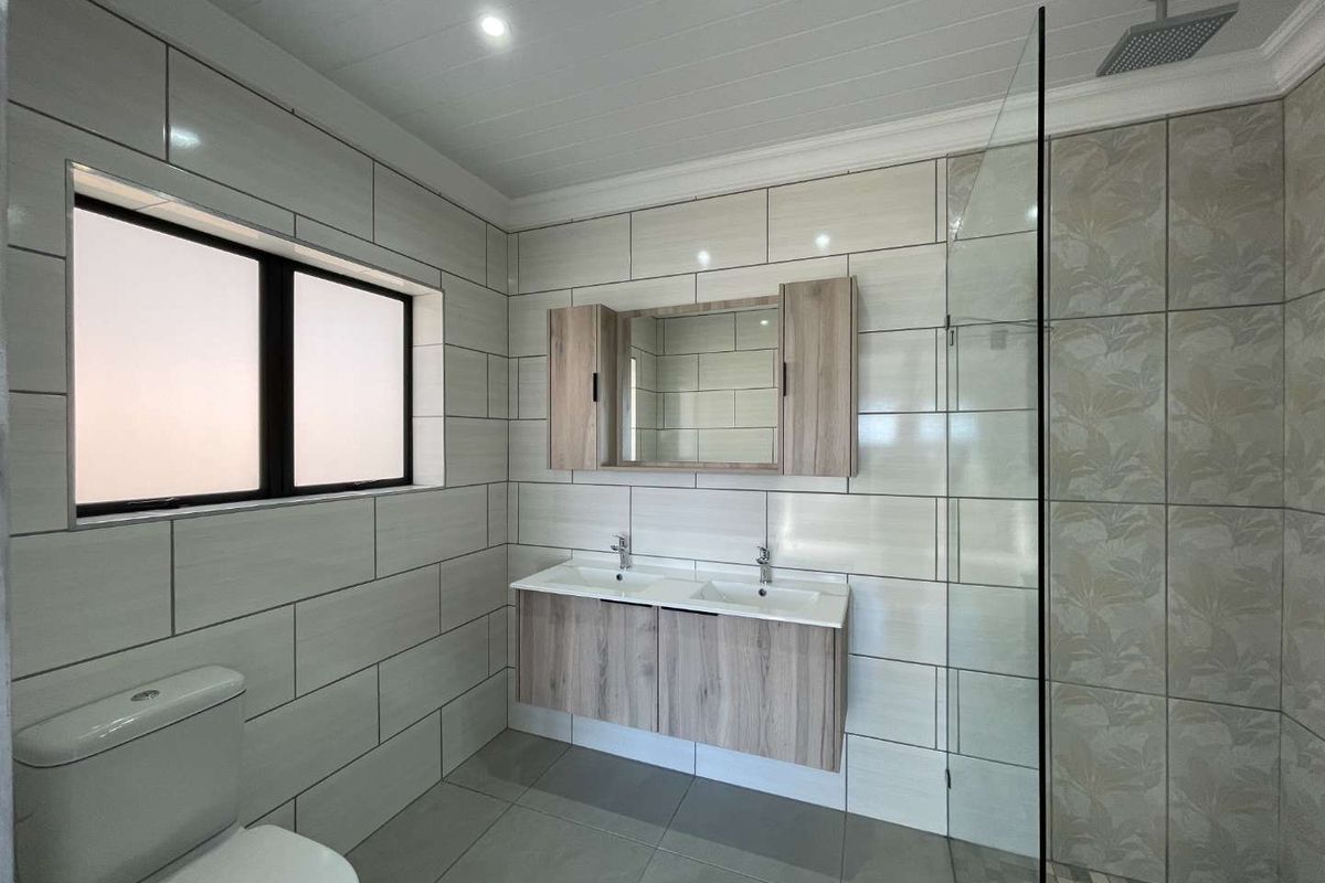 Modern bathroom featuring a double vanity with wood-look cabinetry, a frameless glass walk-in shower with rainfall showerhead, and contemporary wall and floor tiling.
