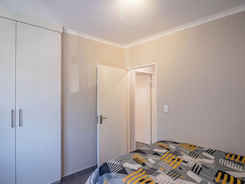 A clean bedroom featuring neutral walls, tiled flooring, and a built-in wardrobe, offering a simple and functional living space.