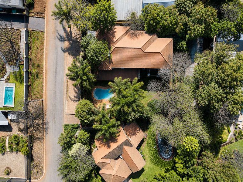 Aerial view of the property showcasing the main dwelling, tiled roof, swimming pool, and established garden surroundings.