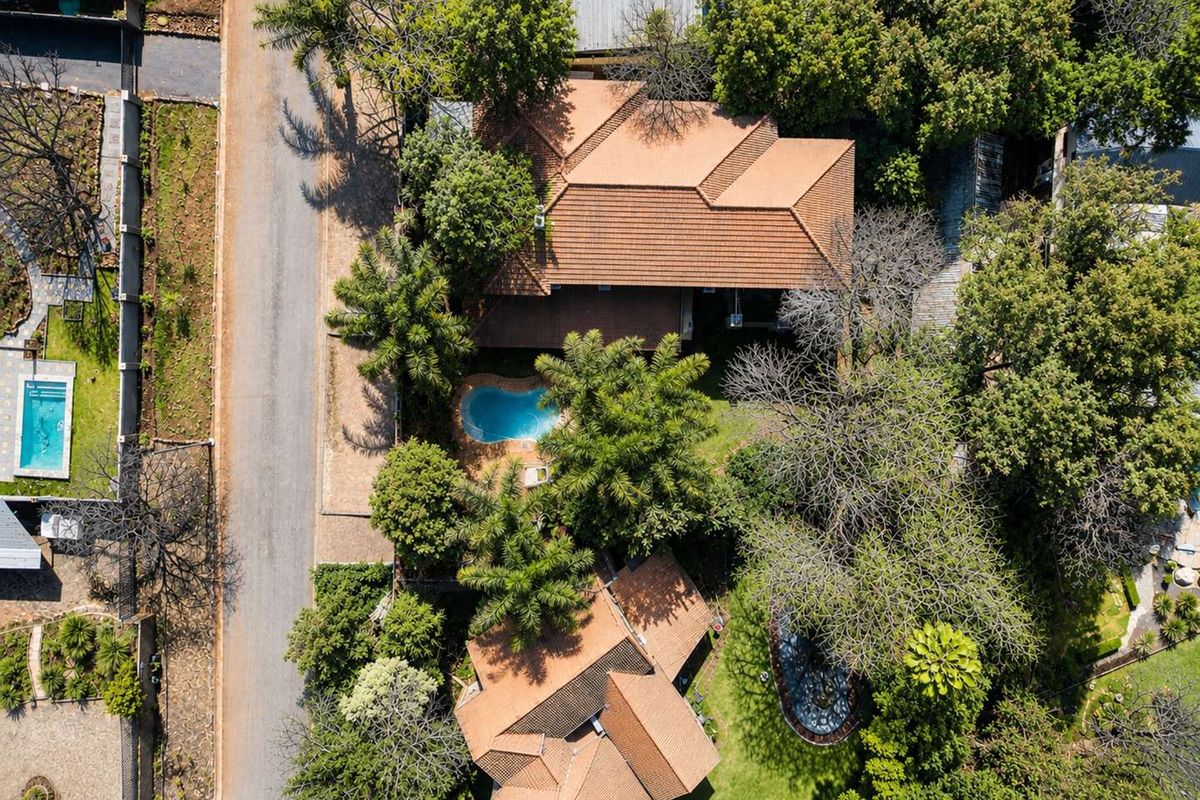 Aerial view of the property showcasing the main dwelling, tiled roof, swimming pool, and established garden surroundings.