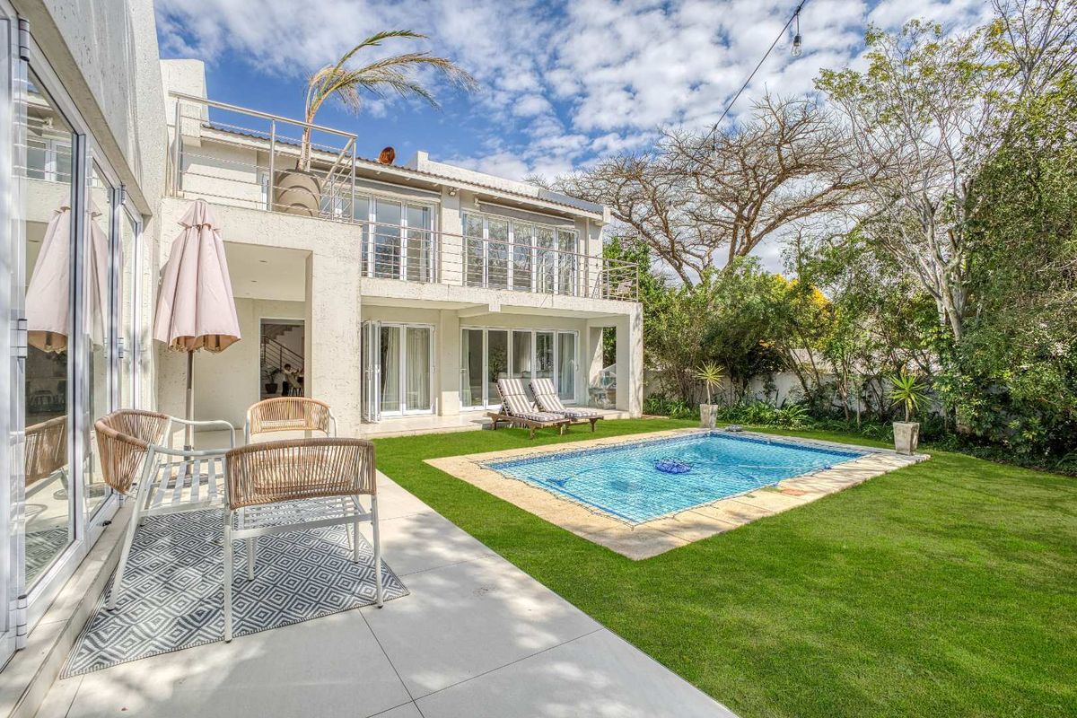 A well-maintained rear exterior featuring a swimming pool, tiled patio area, and a two-story facade with balcony access and large sliding glass doors.