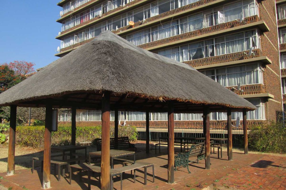 A communal outdoor area featuring a thatched gazebo with timber supports set on a brick-paved patio within an apartment complex.