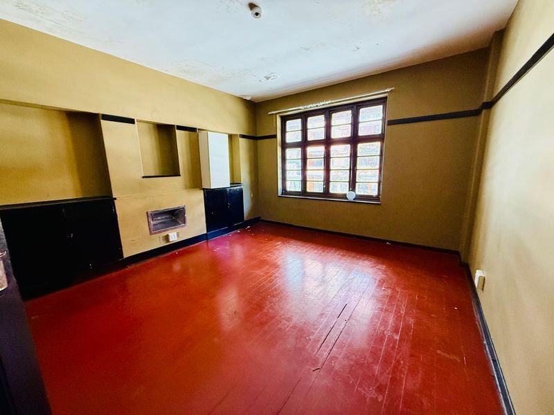 An empty living room featuring painted timber floors, built-in cabinetry, and a fireplace, requiring ceiling repairs and cosmetic updates.