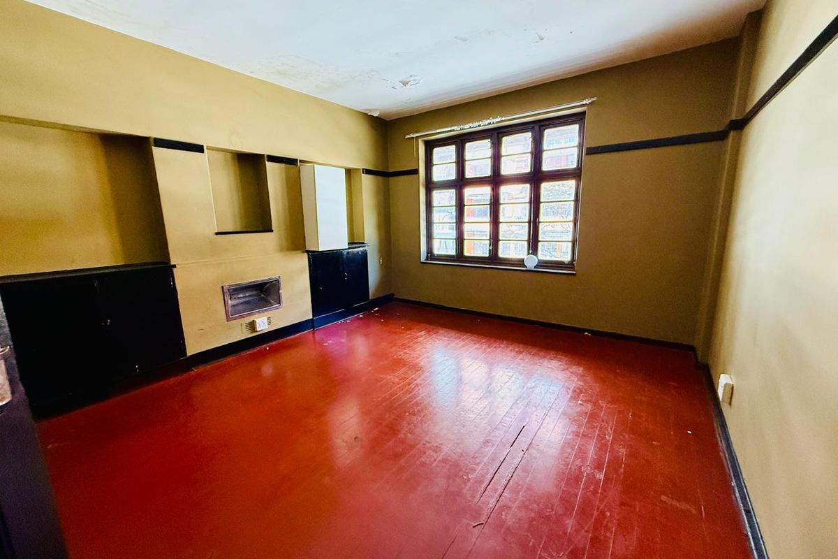 An empty living room featuring painted timber floors, built-in cabinetry, and a fireplace, requiring ceiling repairs and cosmetic updates.