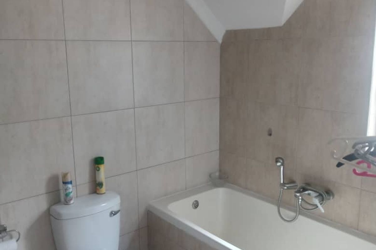 A functional bathroom featuring a built-in bathtub with shower mixer and a standard toilet, finished with neutral wall tiling and a sloped ceiling.