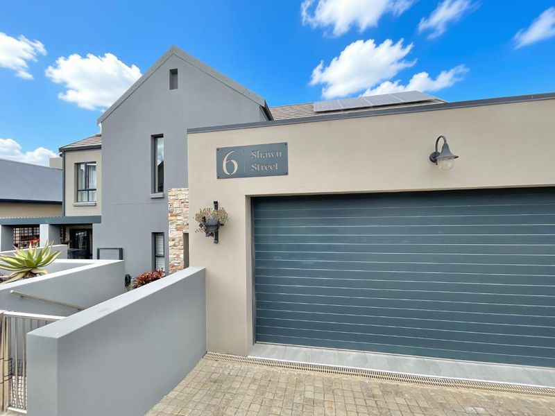 Modern front facade featuring a grey sectional garage door, stone cladding accents, and solar panels installed on the roof.