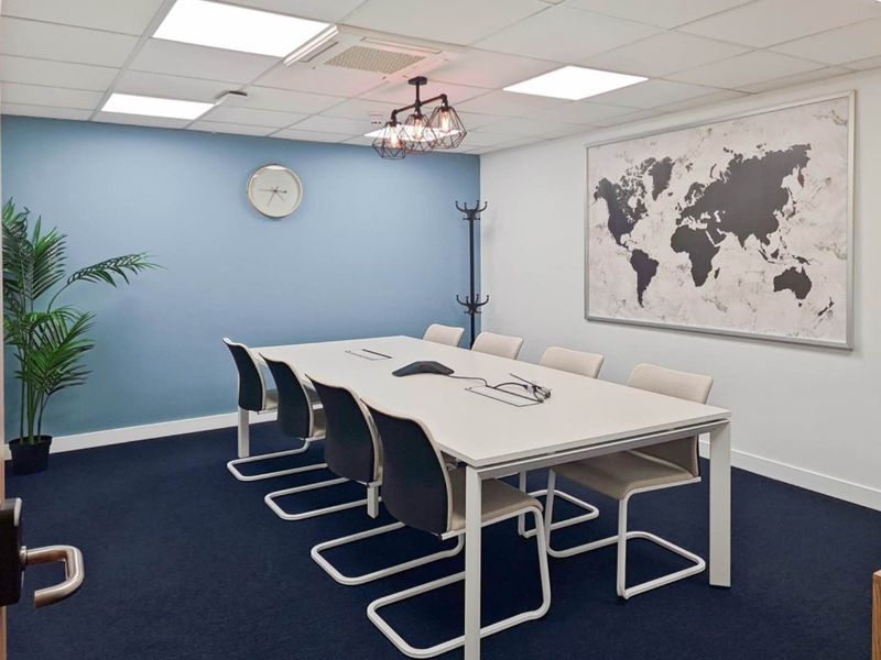 A modern, well-maintained office meeting room featuring a suspended ceiling with integrated lighting, blue accent wall, and dark carpet flooring.
