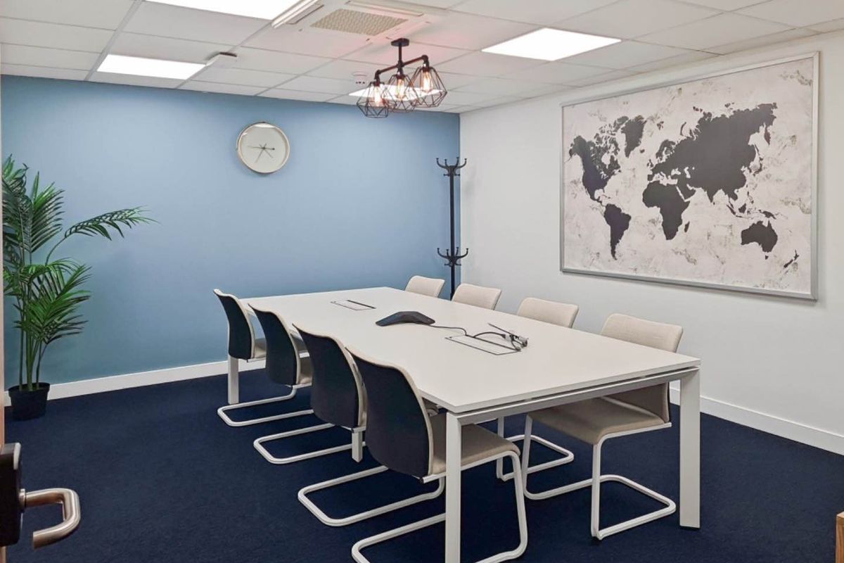 A modern, well-maintained office meeting room featuring a suspended ceiling with integrated lighting, blue accent wall, and dark carpet flooring.