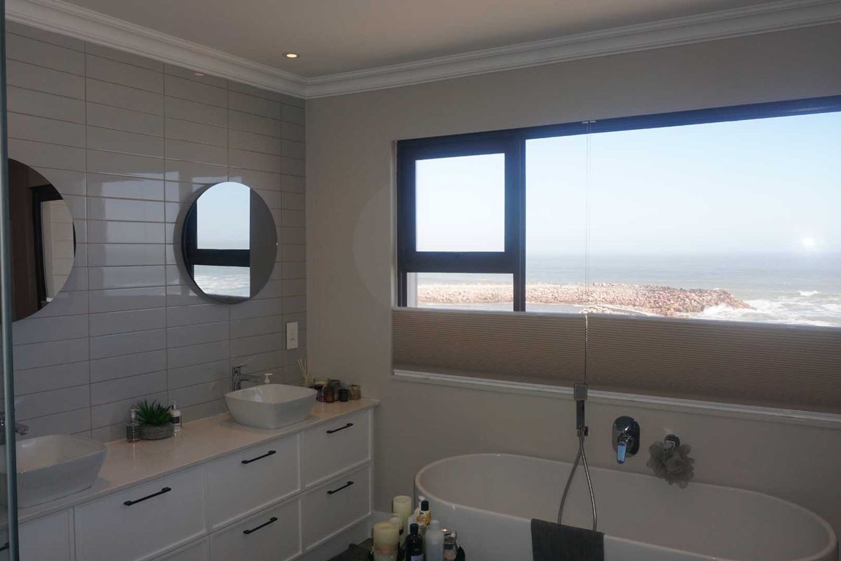 Modern bathroom featuring a double vanity with vessel sinks, a freestanding bathtub, and large windows offering expansive ocean views.