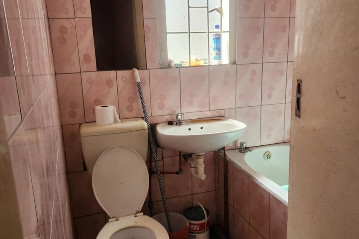 A compact bathroom featuring dated pink wall tiles, a pedestal basin, a toilet, and a built-in bathtub with a window.