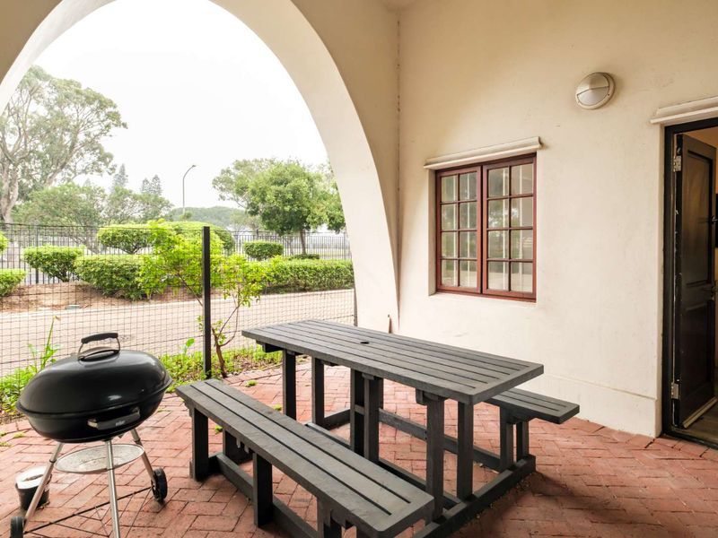A covered patio area featuring brick paving, an arched architectural opening, and direct access to the interior through a timber-framed door.