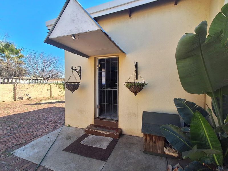 Rear exterior view featuring a paved patio area, security gate entrance, and a protective awning over the doorway.
